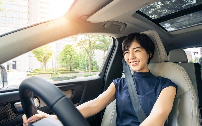 Smiling woman driving a car on a sunny day with seatbelt fastened.