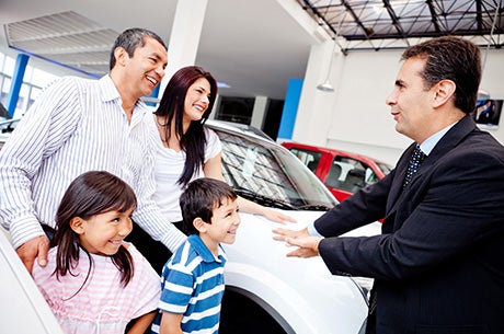 A smiling family receives their new car from a salesperson.