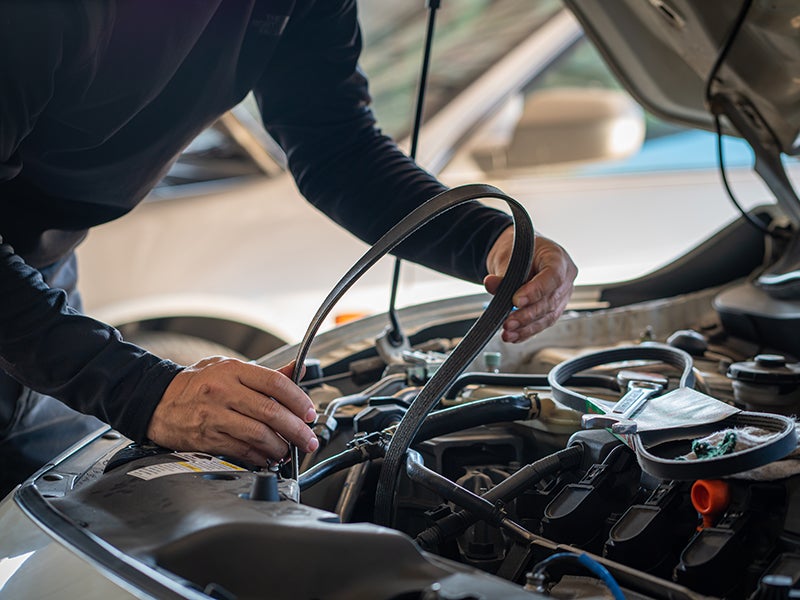A mechanic working under the hood of a car, inspecting or replacing a serpentine belt.