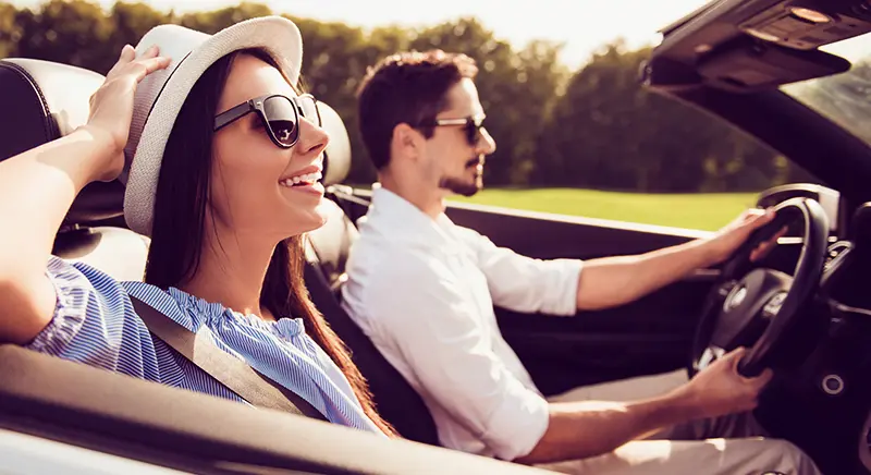 A smiling man sits in the driver’s seat of a car and girl beside him.